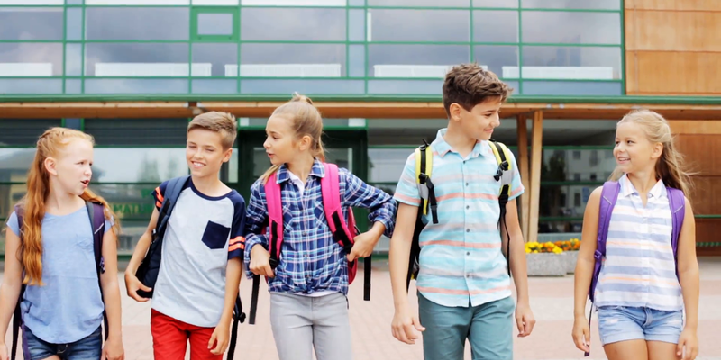 Medium primary education communication and people concept group of happy elementary school students with backpacks walking and talking outdoors rhotuufy  f0000